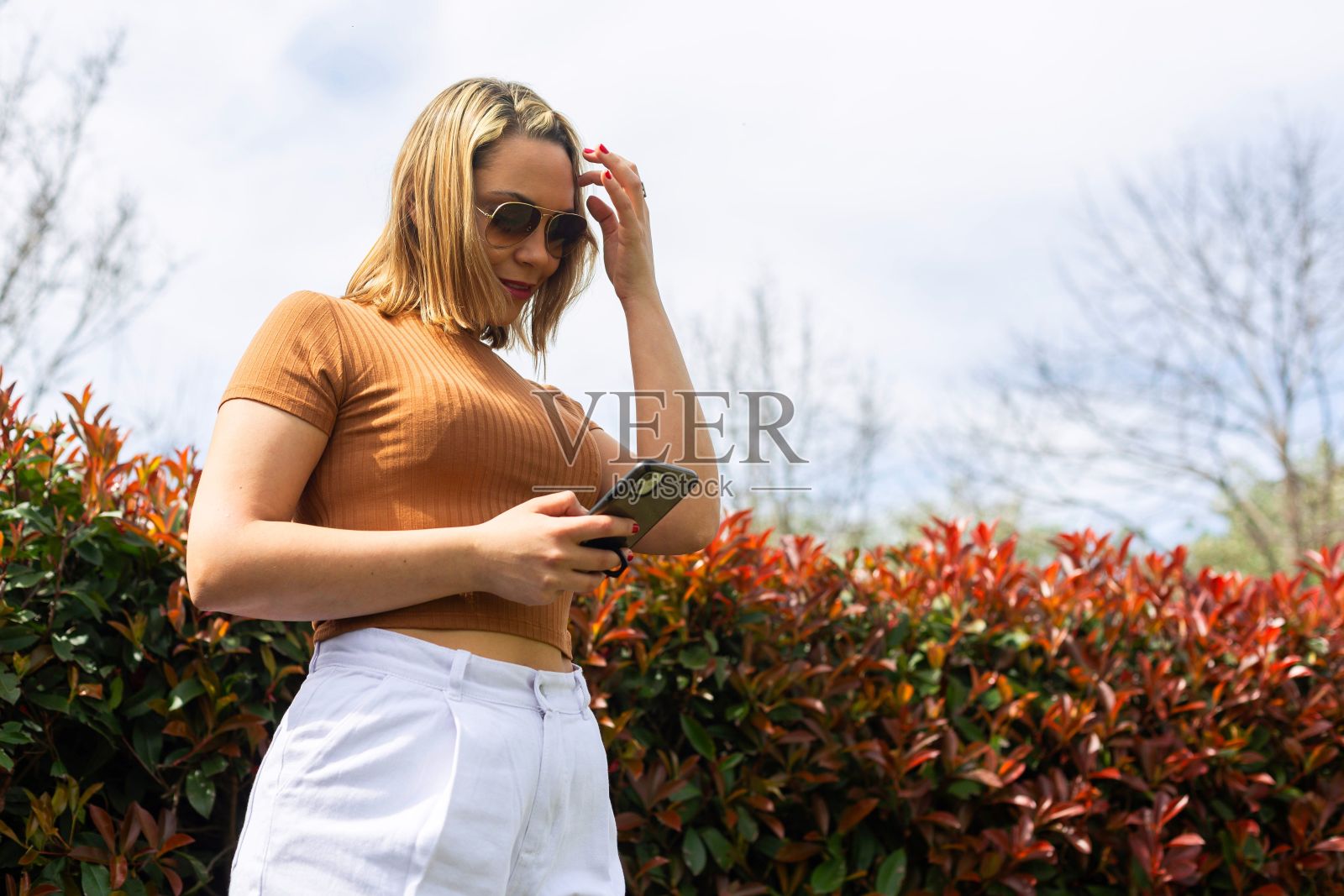 一个微笑的年轻女子在公园里拿着手机的美丽照片照片摄影图片