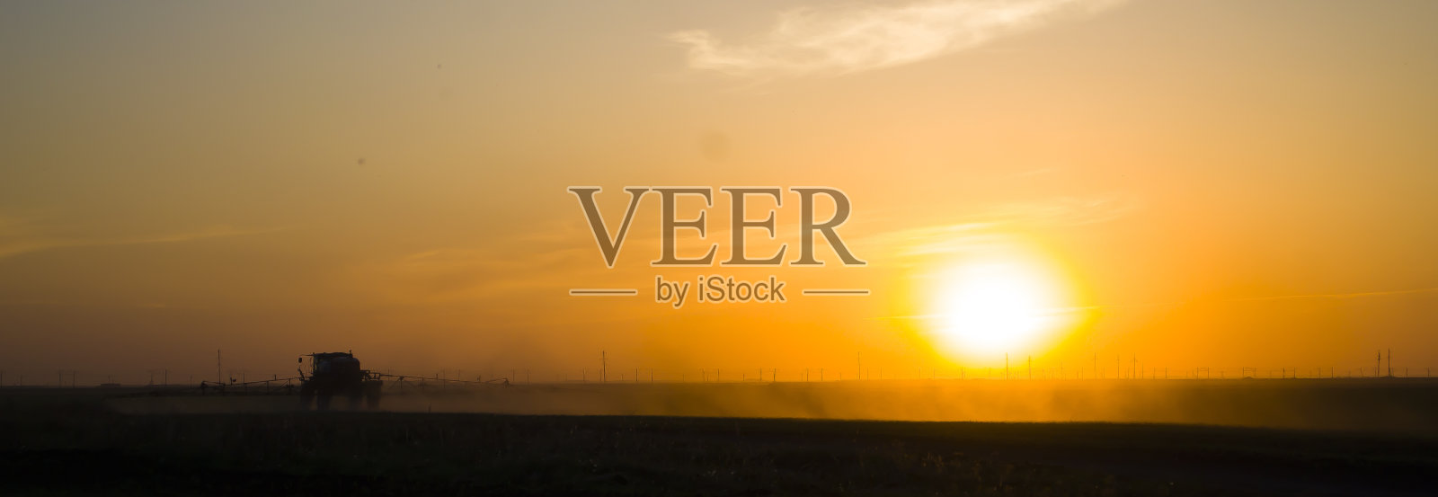 日落时分，田里的拖拉机在洒水，这对辛勤的工人来说是艰难的一天。田间病虫害的化学处理。现代agroculture。照片摄影图片