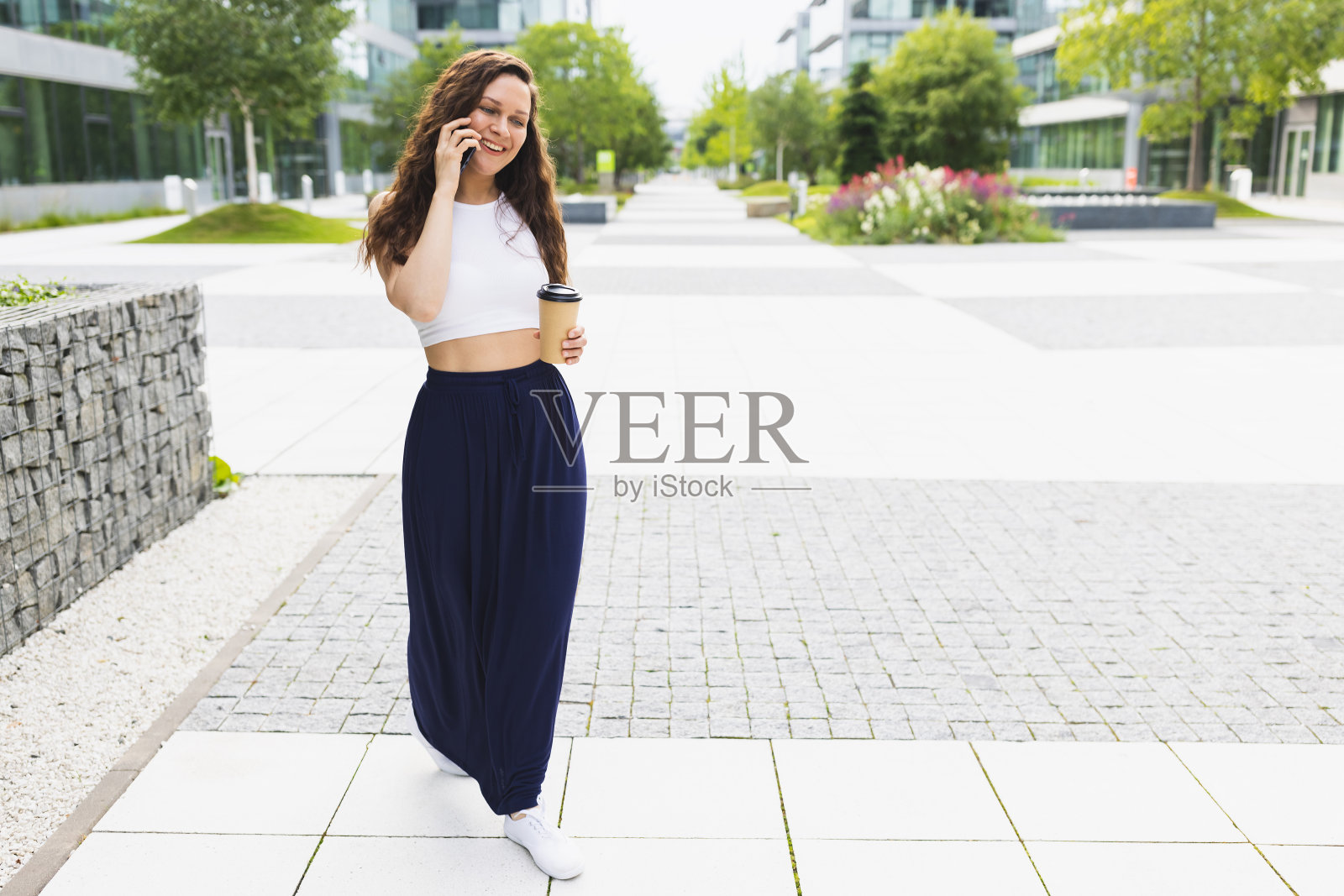 快乐的女人端着咖啡打电话，走在城市的街道上，复制空间照片摄影图片