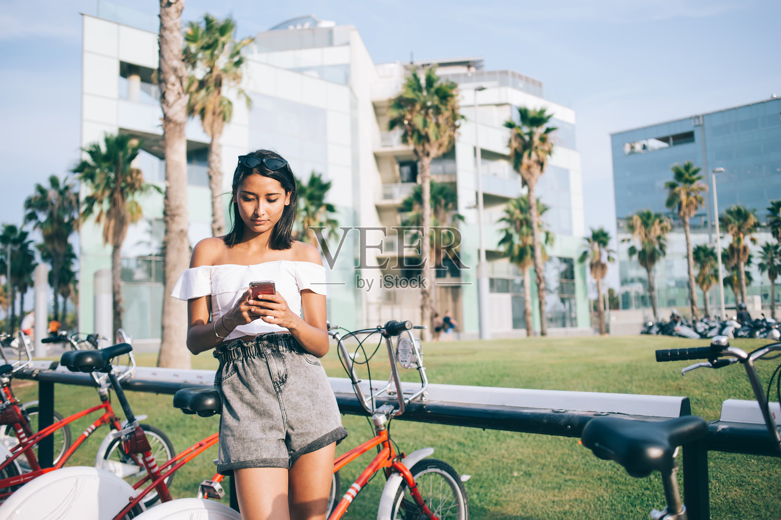 时髦的女人，手机在自行车停放在现代城市照片摄影图片