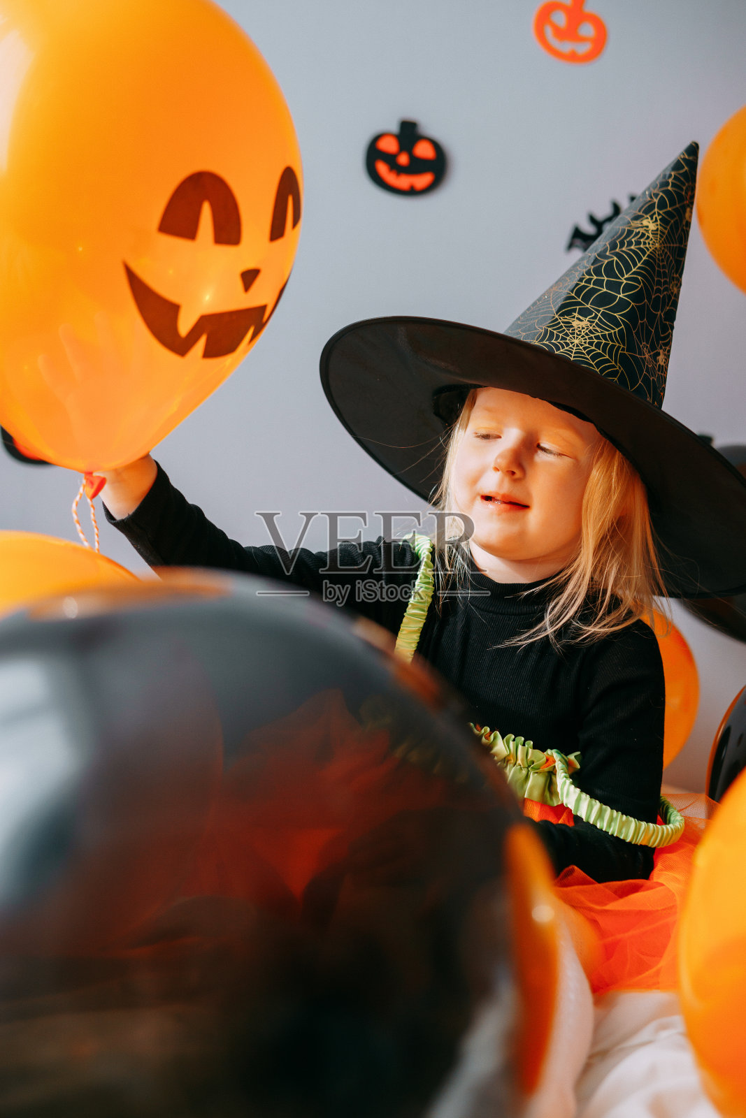 孩子们的万圣节——一个戴着女巫帽和狂欢节服装的女孩，在家里放着橙色和黑色的气球。准备好庆祝万圣节了。照片摄影图片