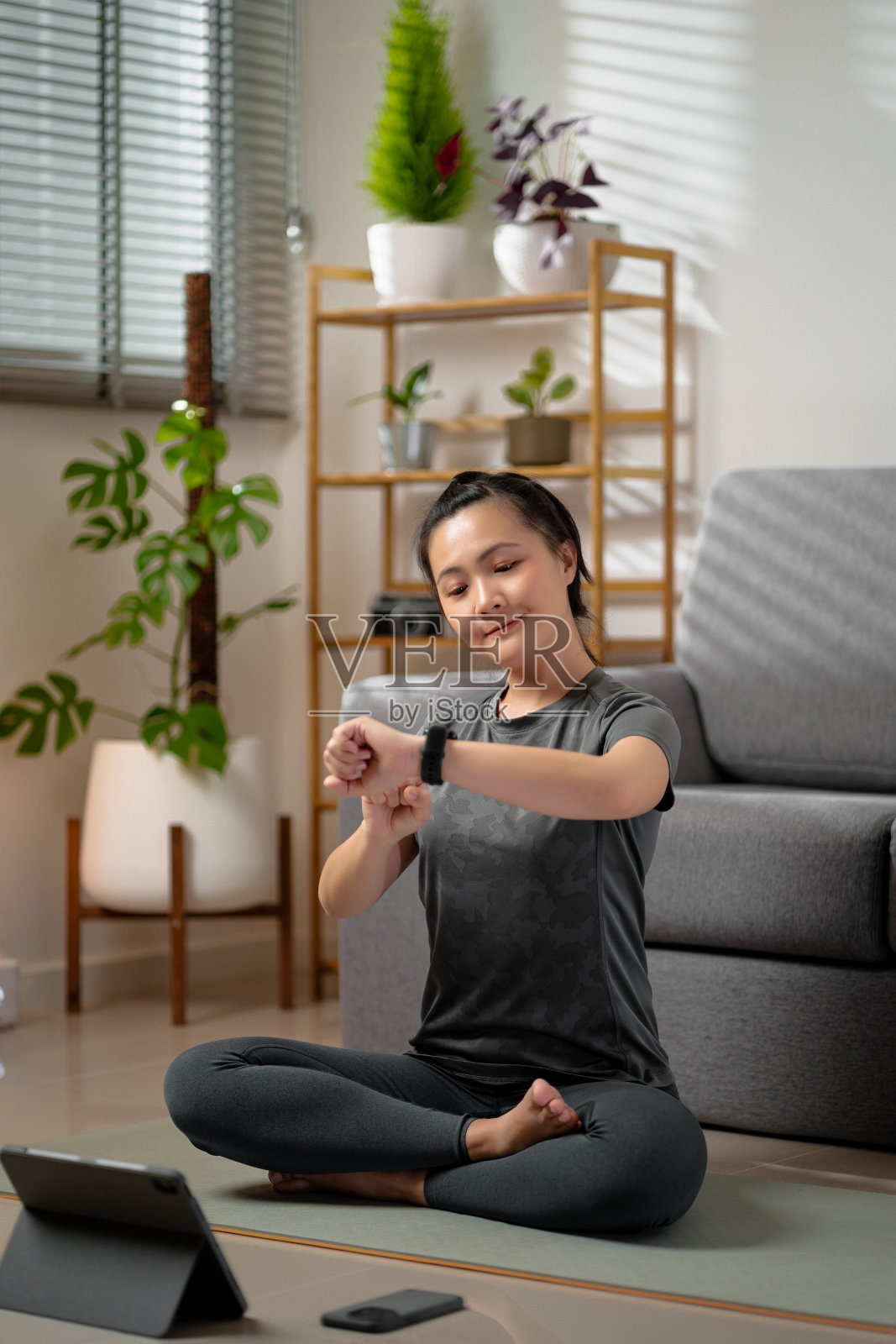 亚洲女性看着智能手表，很高兴锻炼目标成功，在家客厅放松。照片摄影图片