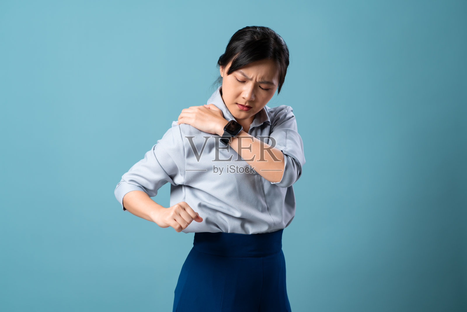 一名肩膀疼痛的亚洲妇女孤立地站在蓝色背景上。照片摄影图片
