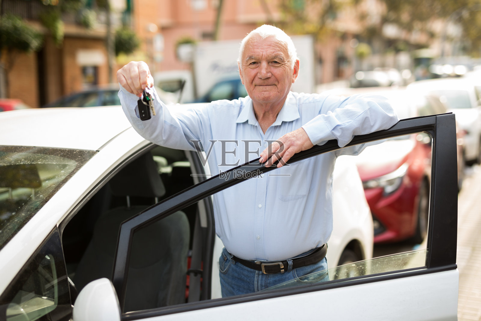 快乐的老人，手里拿着钥匙，在新车旁摆姿势照片摄影图片