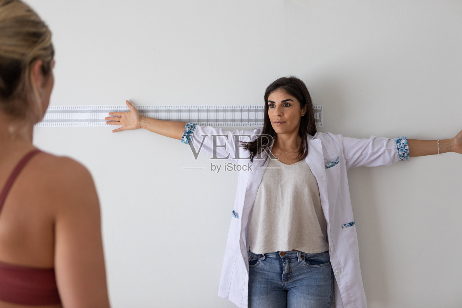女性营养学家和出境学家在医疗咨询期间向女性病人展示如何站起来测量四肢照片摄影图片