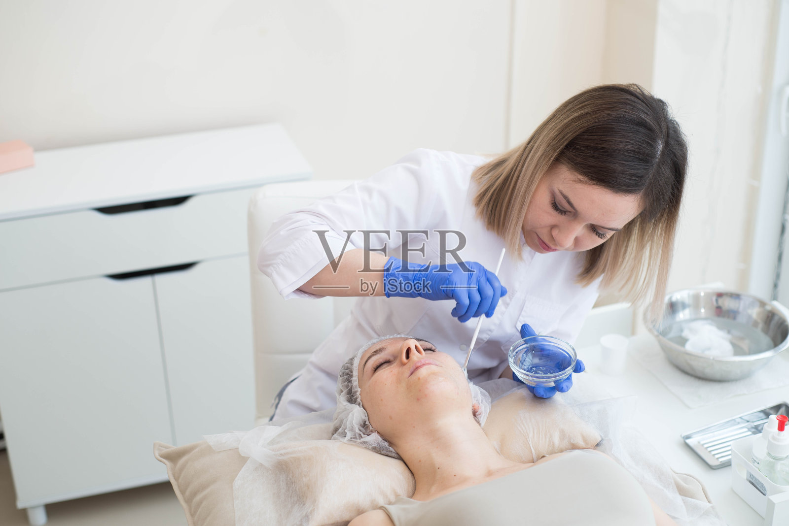 在水疗沙龙里，美容师用刷子把面霜涂在病人脸上照片摄影图片