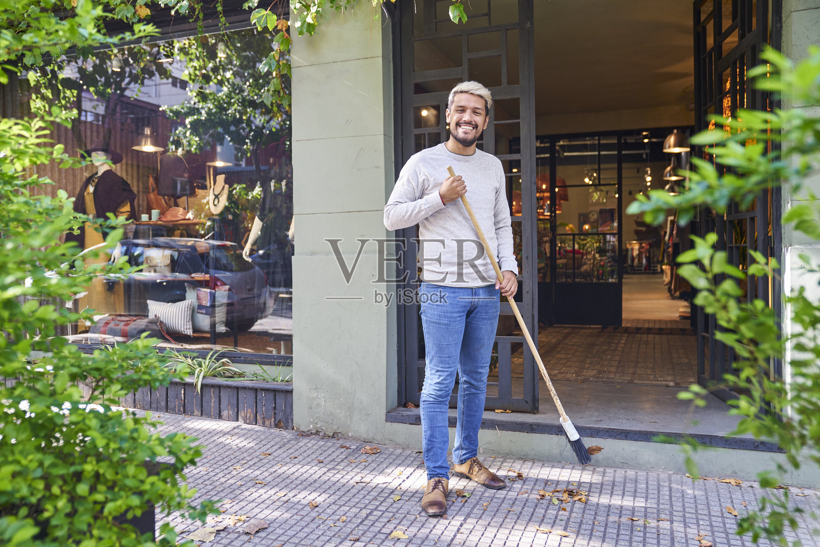 拉丁美洲的精品店工人一边看着镜头，一边用扫帚清扫商店入口照片摄影图片