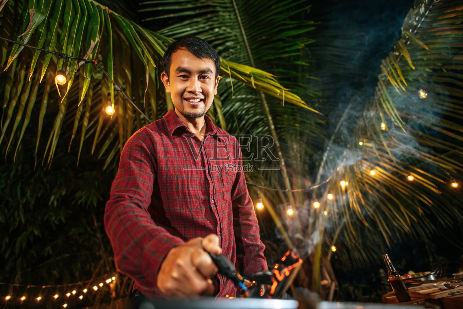 快乐的亚洲年轻人的肖像在烧烤烤架上烹饪肉在新年聚会。Bar-B-Q或在传统炉子上烧烤。晚会、人、庆典概念。照片摄影图片