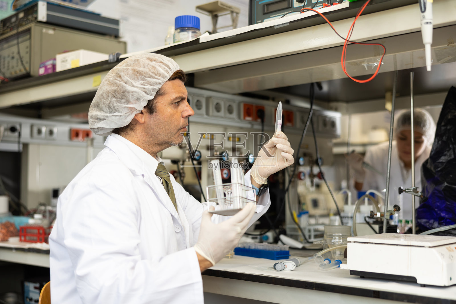 严肃的拉丁男性生物化学家手持三脚架，在研究中心检查试管中的化学反应溶液照片摄影图片