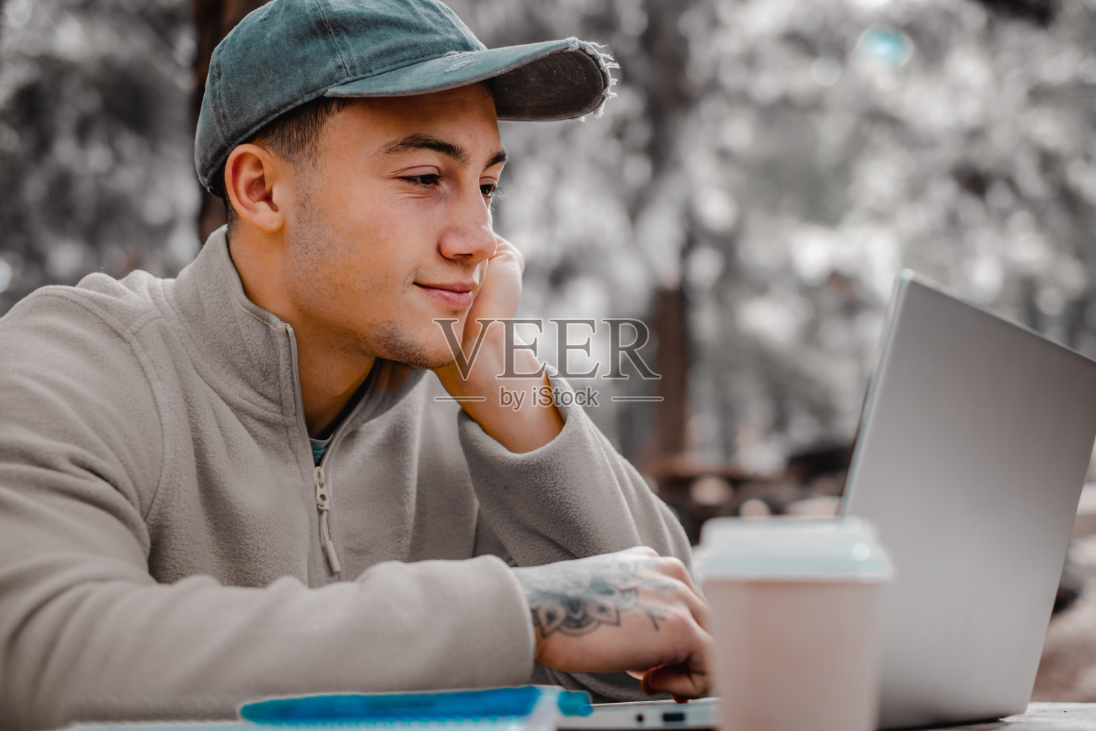 在新鲜空气中做生意。沉思美丽的年轻男子在笔记本电脑上工作，坐在森林里的户外木桌旁。自然智能工作的概念照片摄影图片