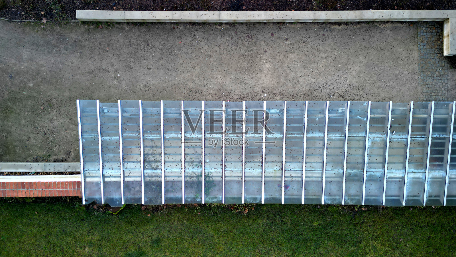 木制结构的凉棚由光滑的圆柱形白色圆柱支撑，是凉亭凉棚的遮蔽物。屋顶内衬玻璃。连接到带砖屋顶、草坪、鸟瞰图的挡土墙照片摄影图片