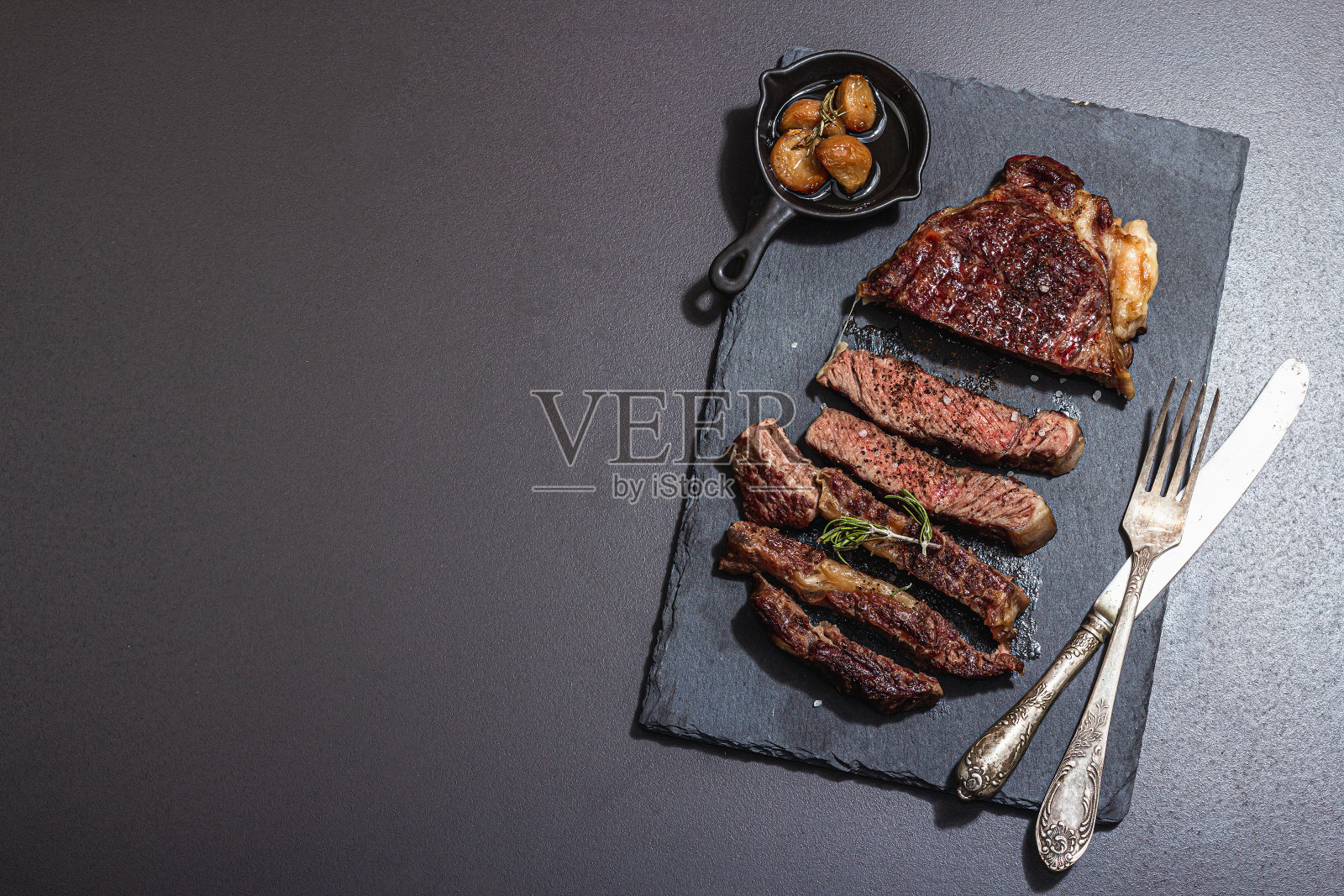 烤熟的肋眼牛排配上焦糖大蒜和老式餐具。硬光，暗影照片摄影图片