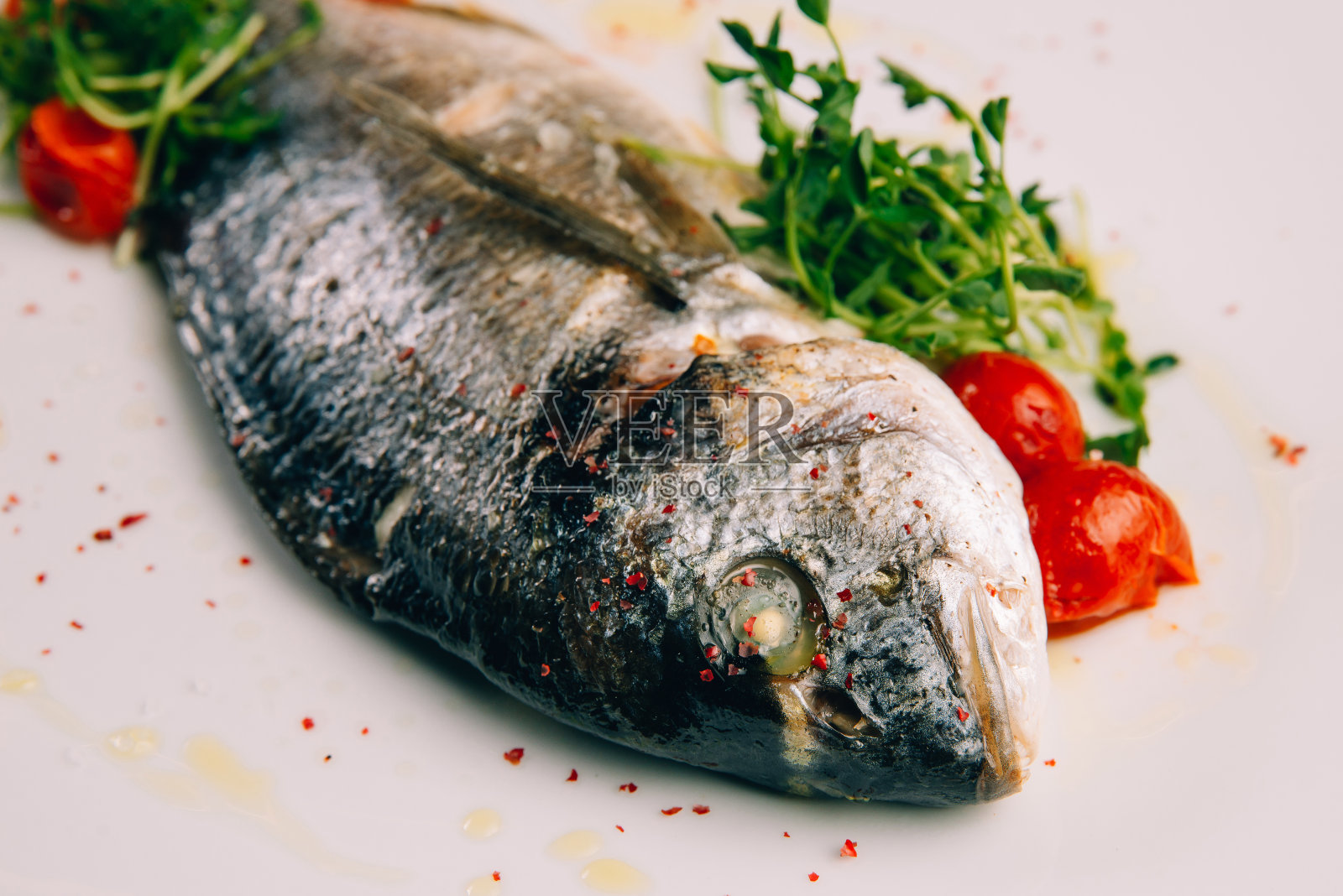 白色盘子里的多拉多鱼配上圣女果和樱桃。照片摄影图片