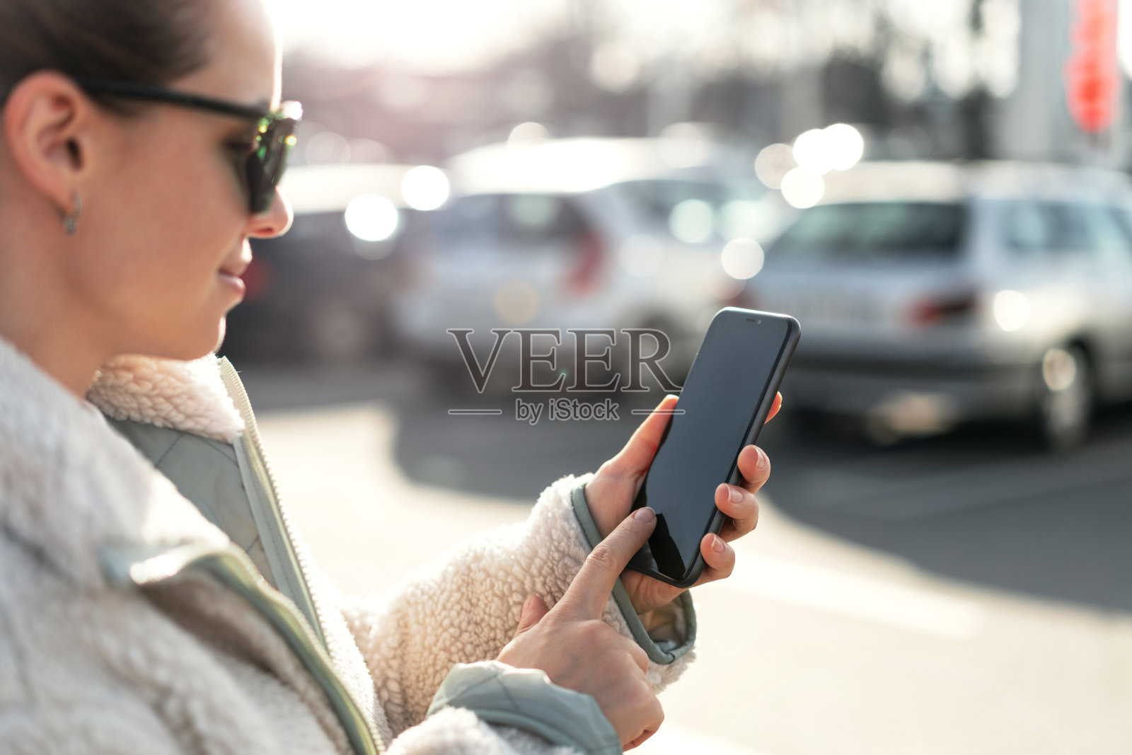 一名女子站在停车场上用手指触摸智能手机屏幕。照片摄影图片