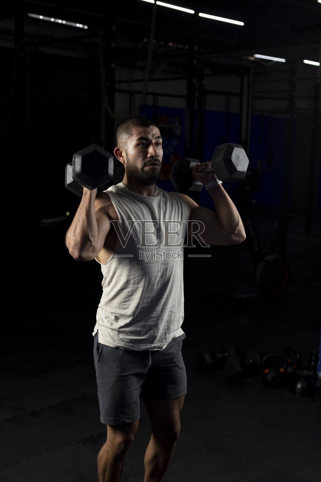 一个肌肉发达的男人的垂直形象，与一对哑铃压在健身房照片摄影图片
