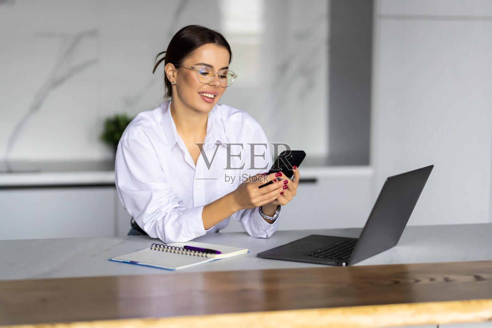 年轻快乐的女人用笔记本电脑在厨房工作用电话照片摄影图片