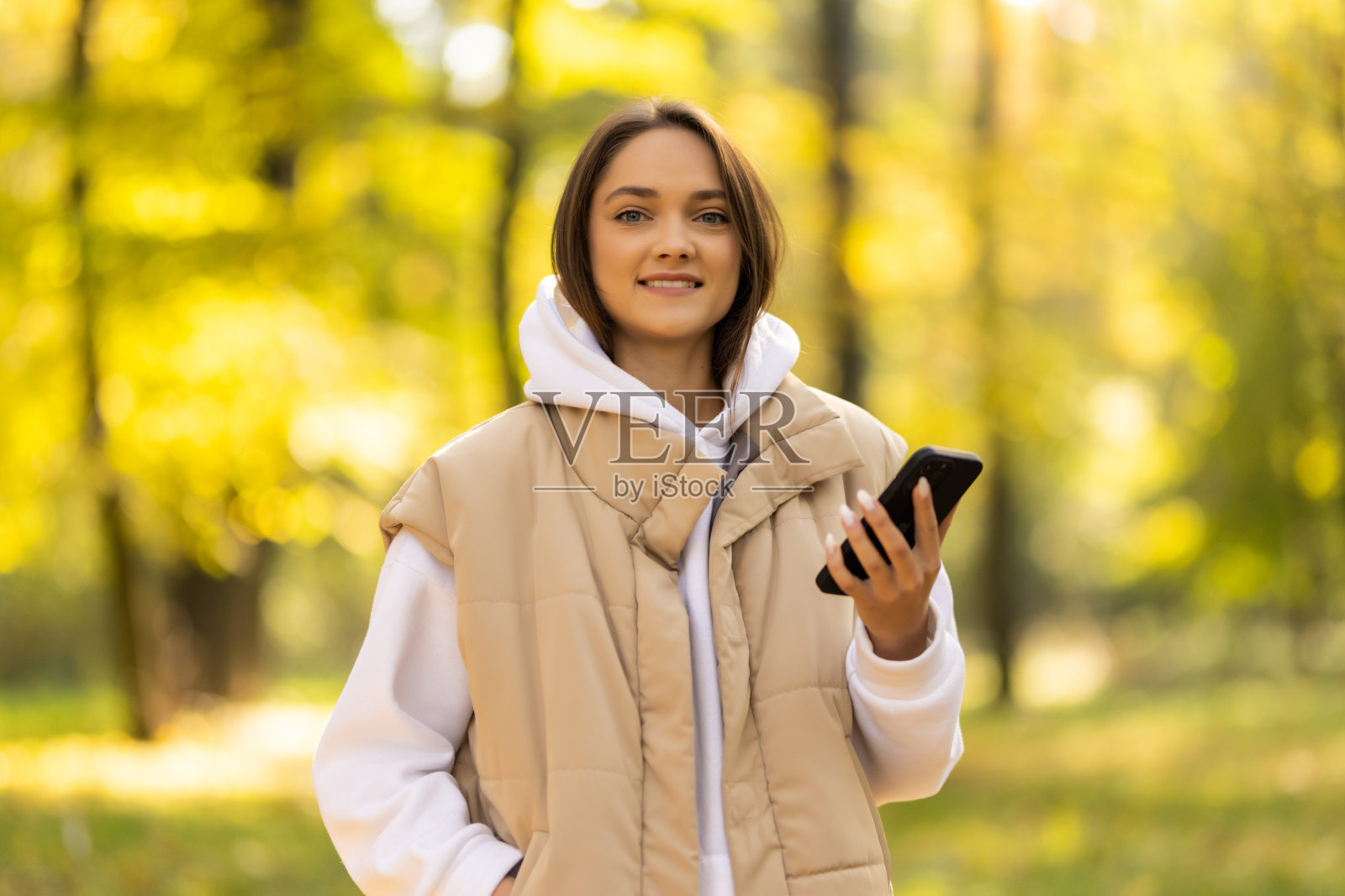 快乐的年轻女子在秋天日落时查看智能手机照片摄影图片