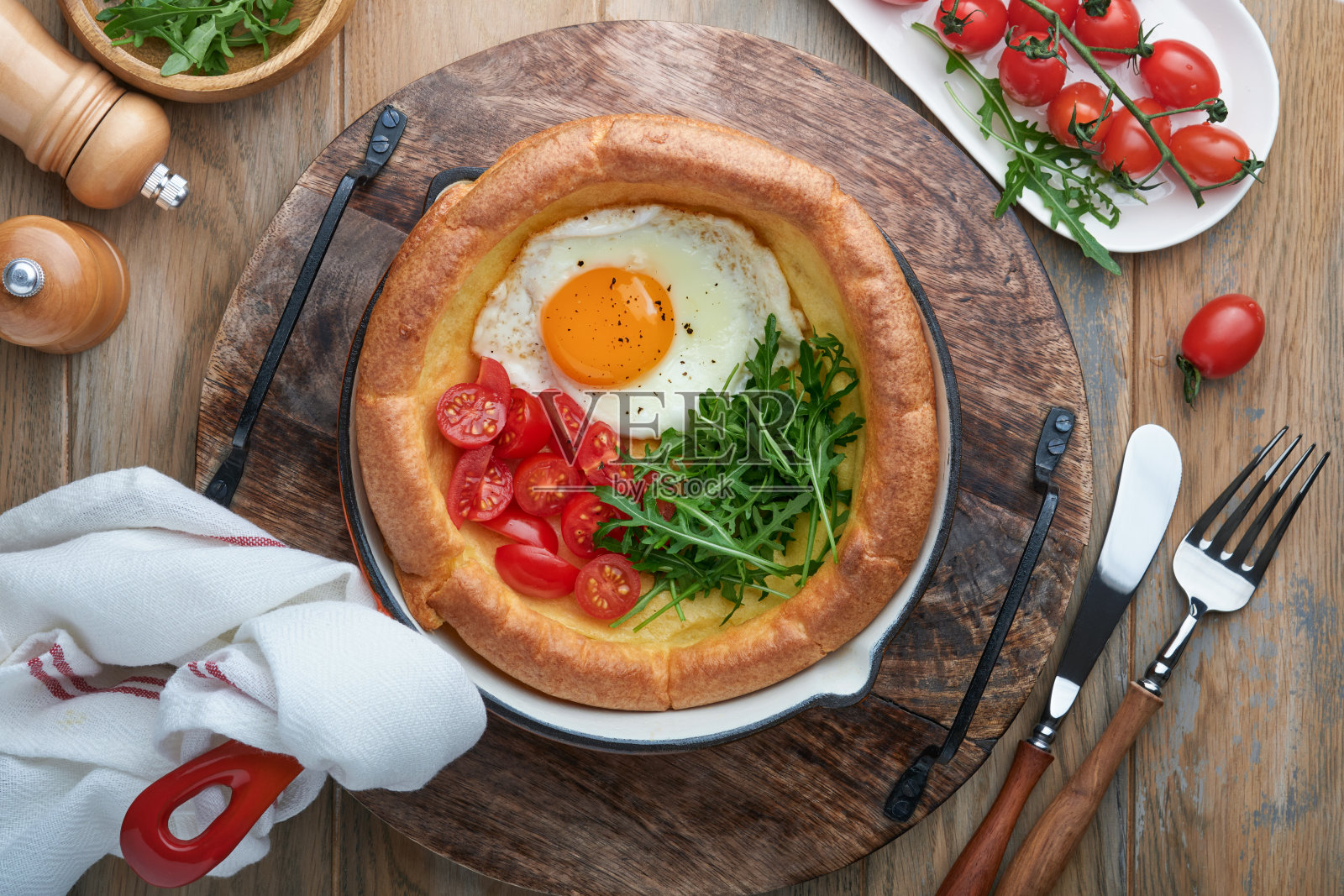 荷兰婴儿煎饼。新鲜自制荷兰婴儿煎饼煎蛋，西红柿和绿芝麻菜在芦苇铸铁锅在旧木桌上。平躺，靠近点。照片摄影图片