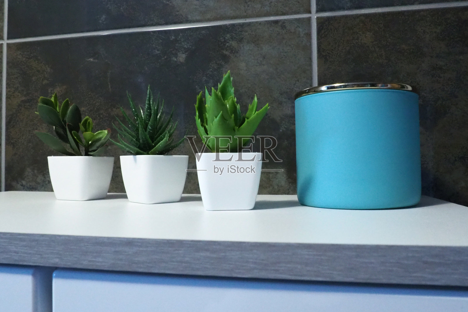 浴室装饰元素。一个蓝色的奶油或油罐，白色的小罐子里装着绿色的人造植物。黑色墙砖。卫生间内饰照片摄影图片