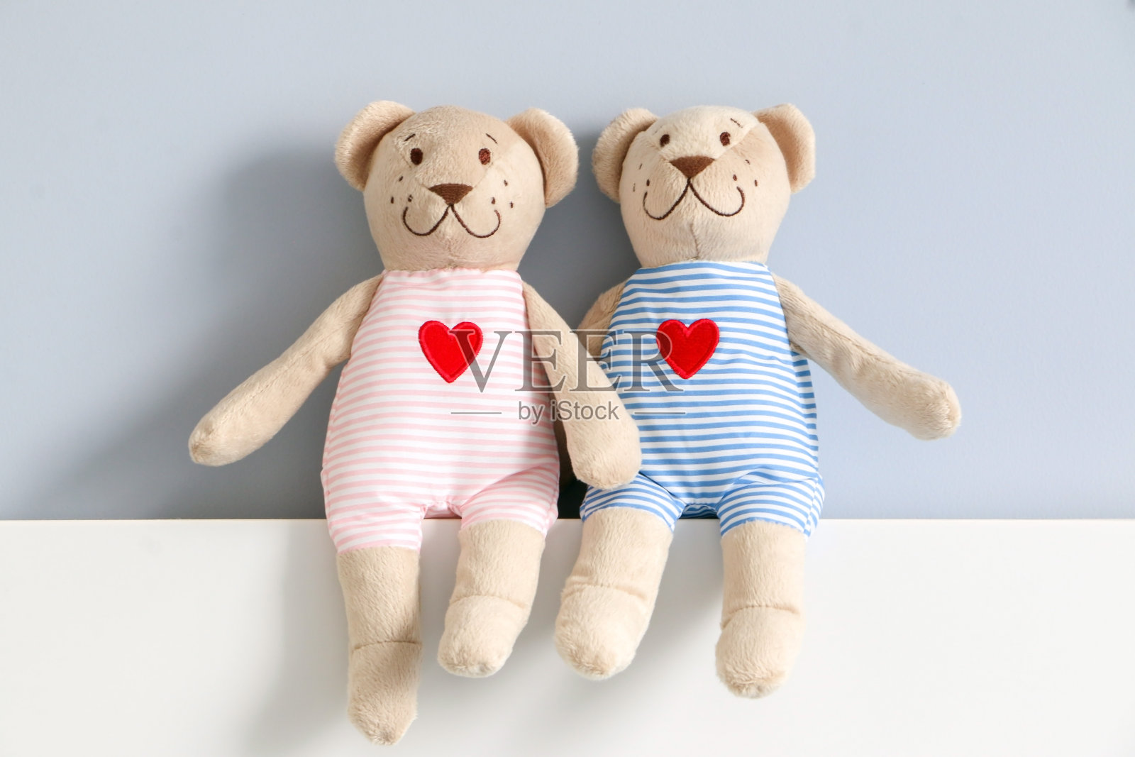 他和她的泰迪熊夫妇穿着浅粉色和蓝色条纹的衣服，有红心图案，坐在床床头板上，背景是浅蓝色的墙壁。填充玩具装饰。照片摄影图片