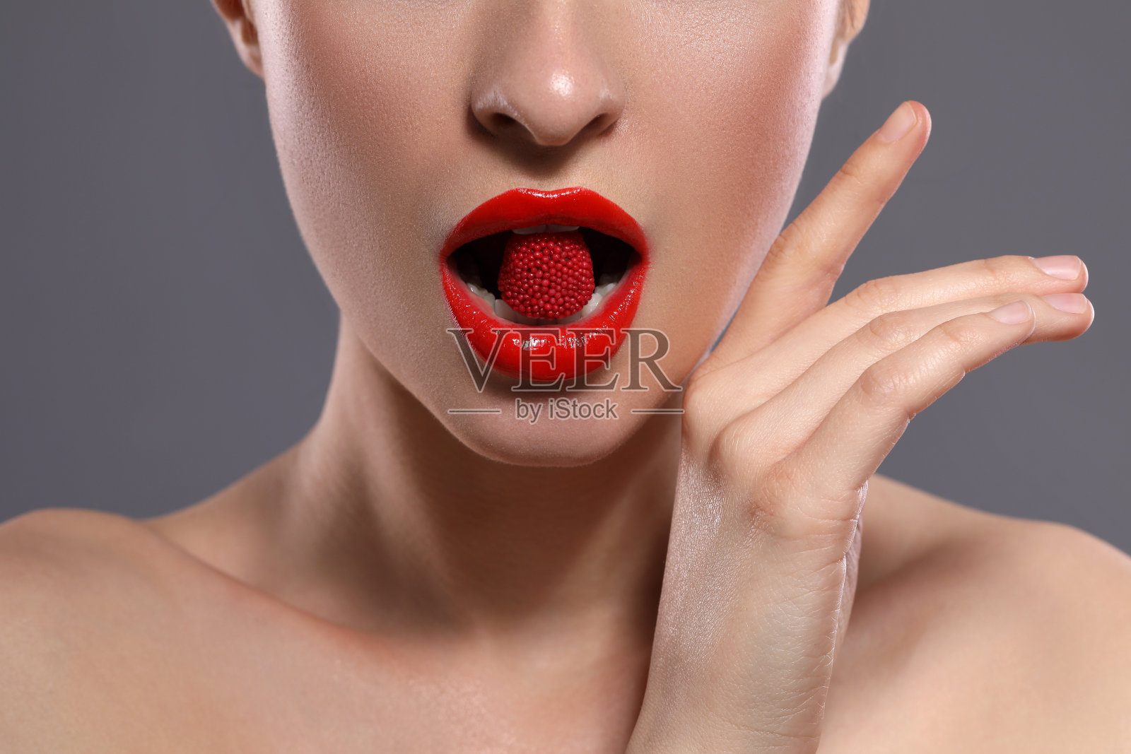 红唇妆的年轻女子在灰色背景上吃糖果，特写照片摄影图片