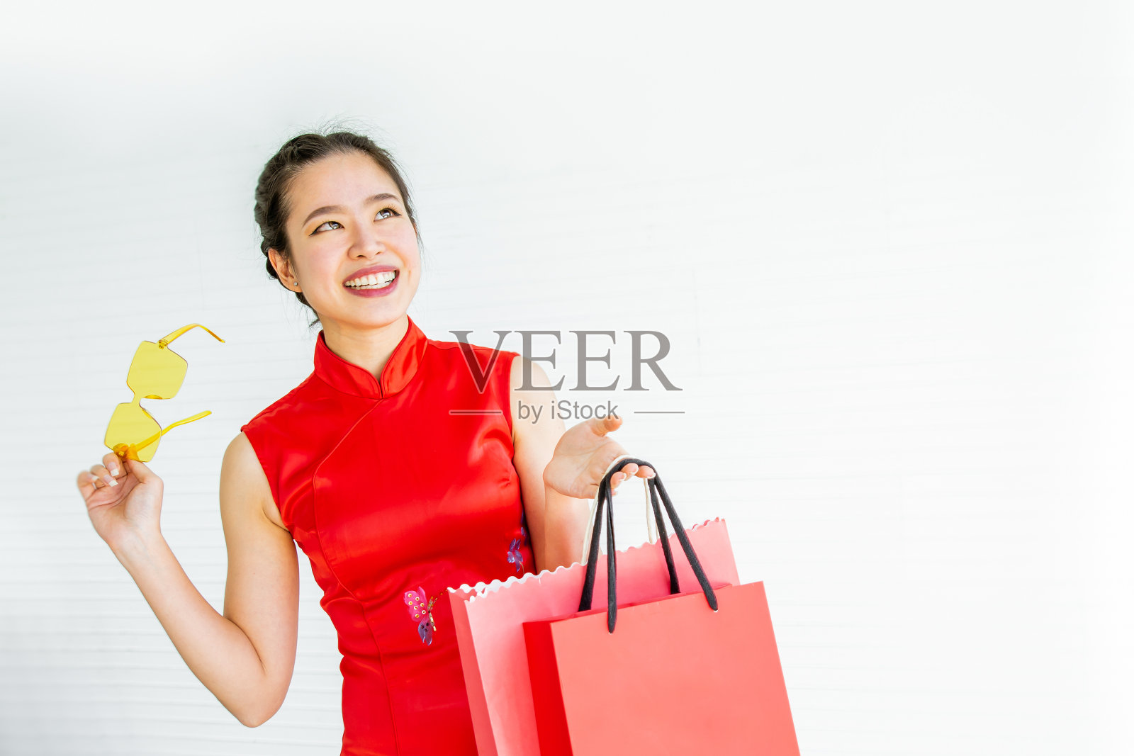 肖像美丽开朗快乐的亚洲妇女穿着红色服装，微笑着，拿着购物袋在白色背景与复制空间，目前促销广告，庆祝中国新年照片摄影图片