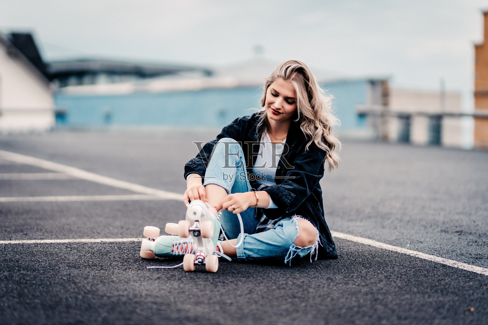 年轻美丽的金发美女穿着黑色夹克和牛仔裤坐在德国郊外的停车场里照片摄影图片