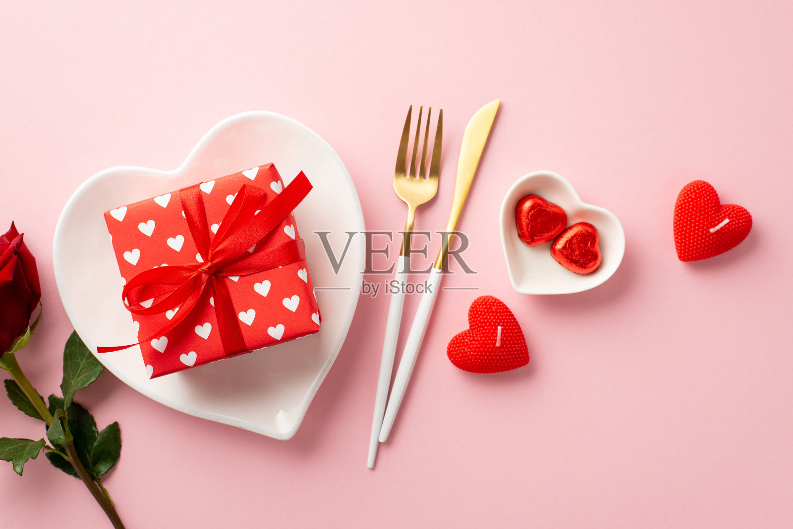 情人节的概念。顶部视图照片的心形菜肴目前盒餐具巧克力糖果玫瑰和蜡烛在孤立的粉彩粉红色背景照片摄影图片