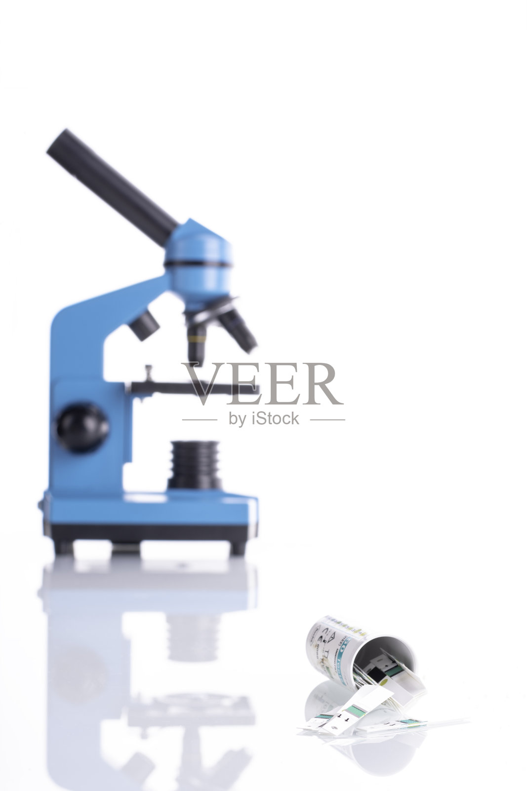 血糖测试箱与测试人员洒在前景白色反光玻璃与蓝色模糊显微镜在背景。照片摄影图片