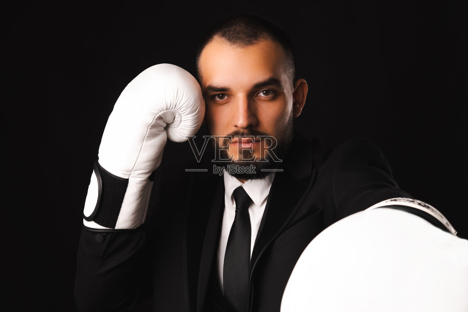 严肃的年轻人穿着黑色西装和拳击手套准备战斗。照片摄影图片
