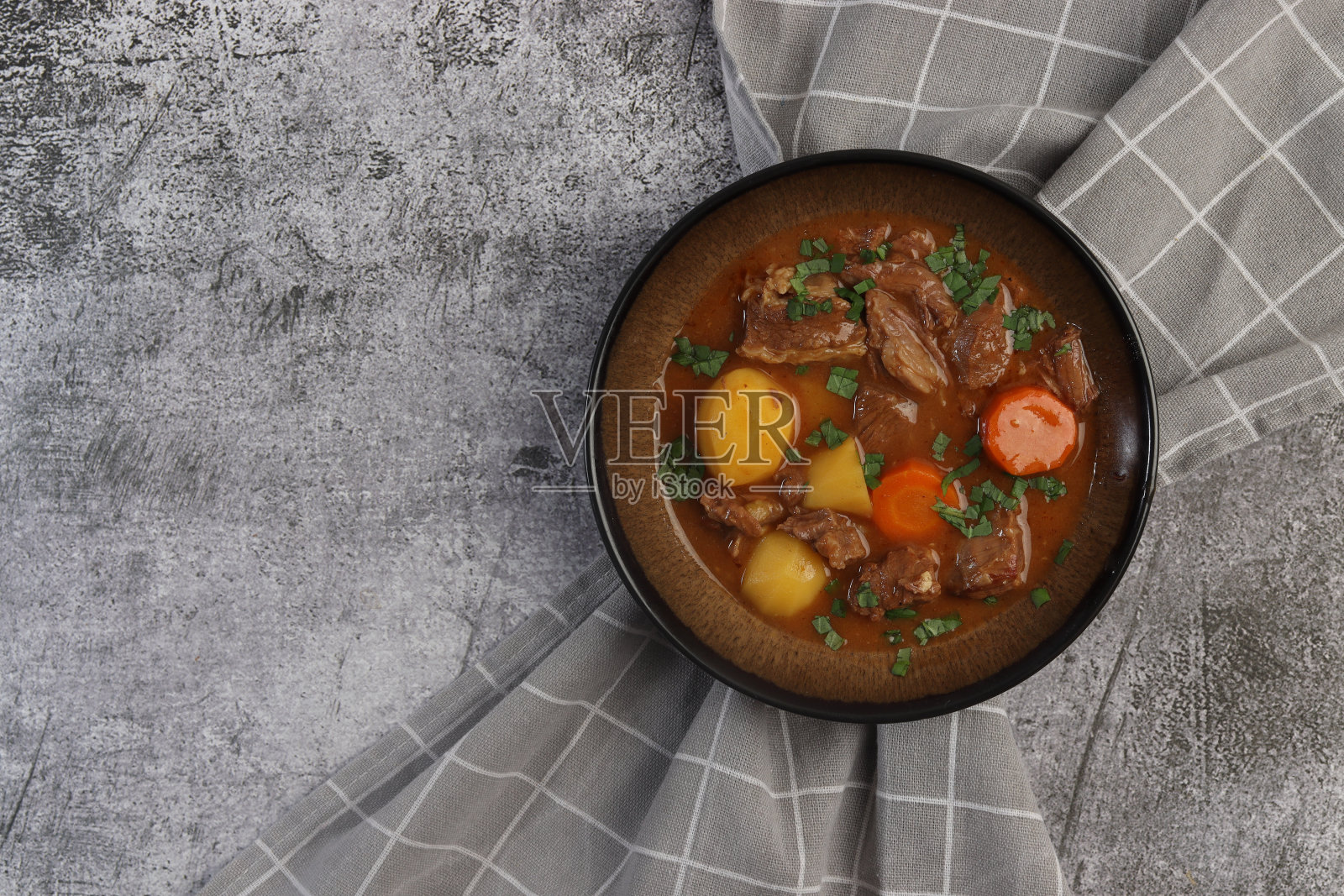 炖牛肉与胡萝卜，土豆和绿色蔬菜在碗里，在黑暗的背景。俯视图，平面布局照片摄影图片