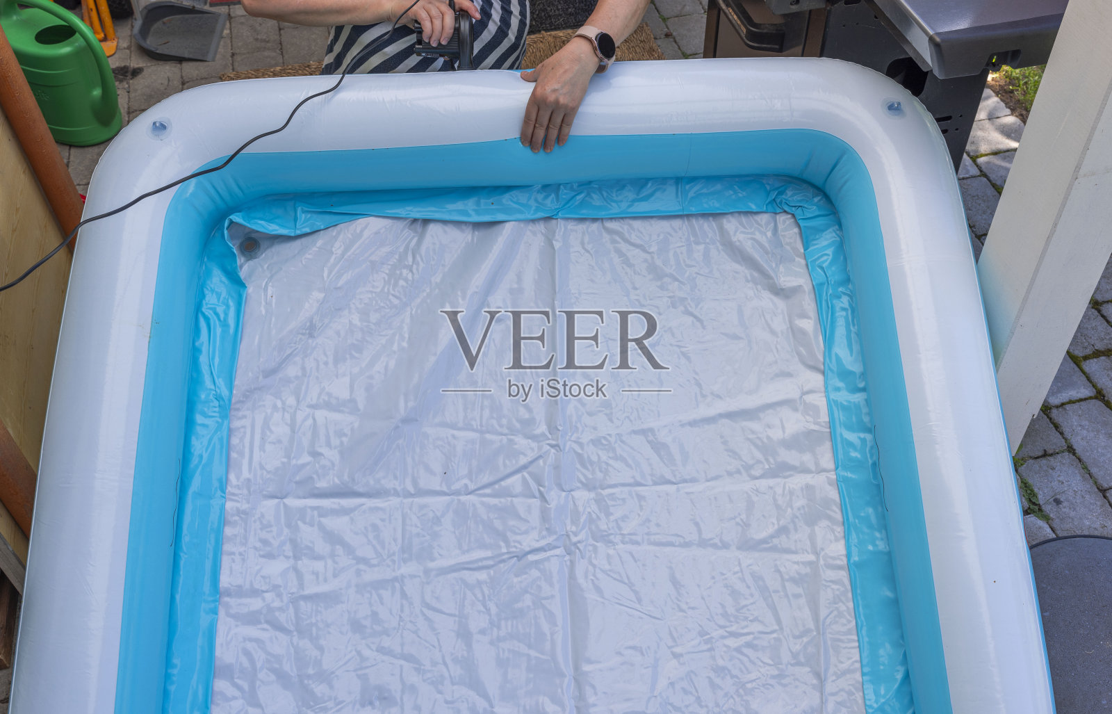 妇女用电动泵给儿童充气池充气。瑞典。照片摄影图片