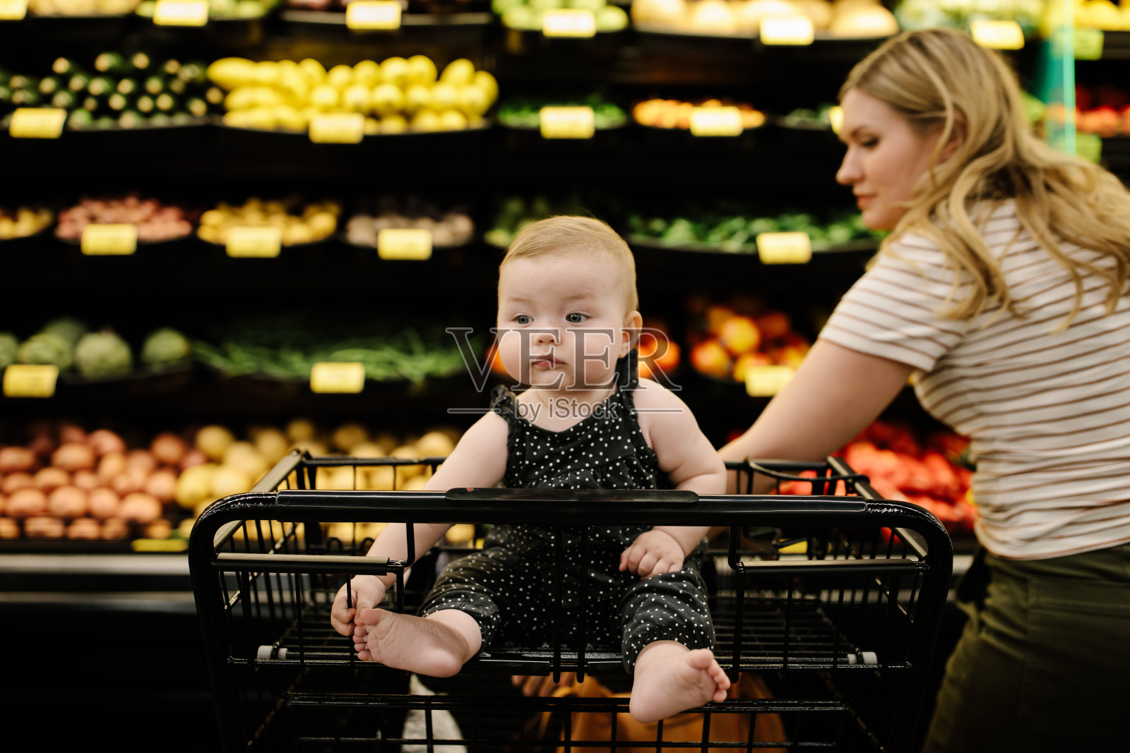 可爱的女婴坐在手推车上，而她的妈妈正在杂货店购物照片摄影图片