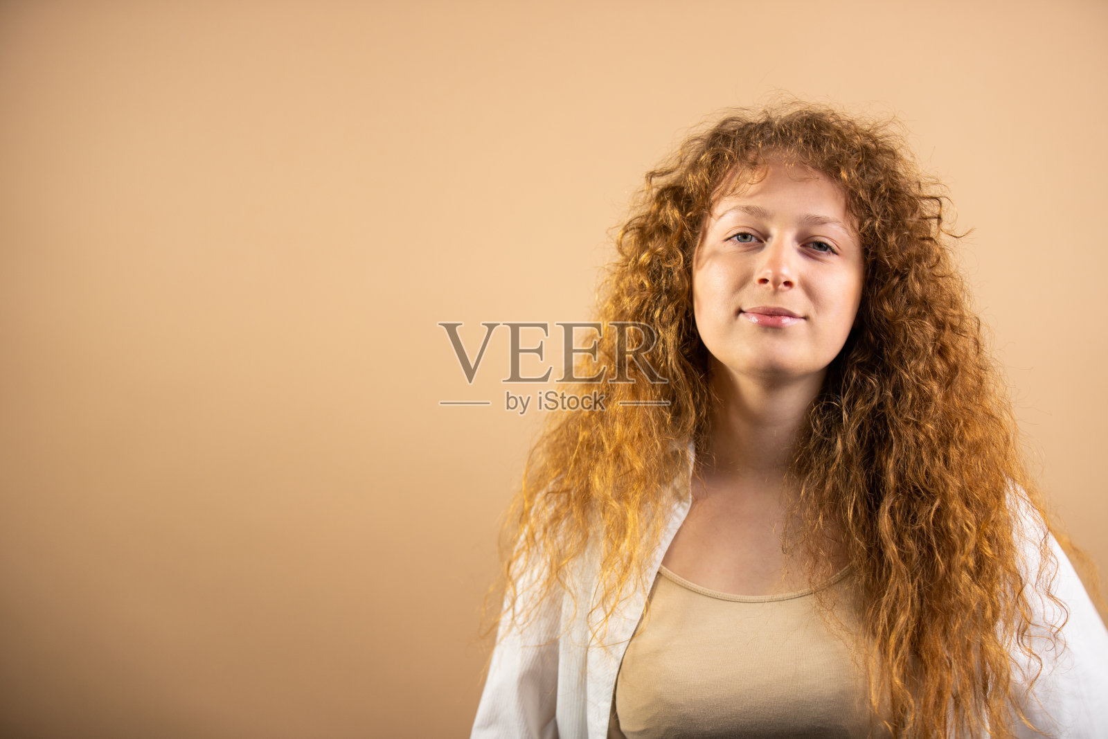 自信的美女与红色长卷发与迷人的外表站在相机与复制空间金色烘焙地面摆姿势。照片摄影图片