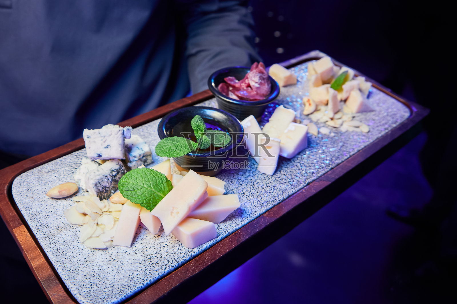 服务员端着一个装着坚果和蜂蜜的奶酪盘，放在木板上照片摄影图片