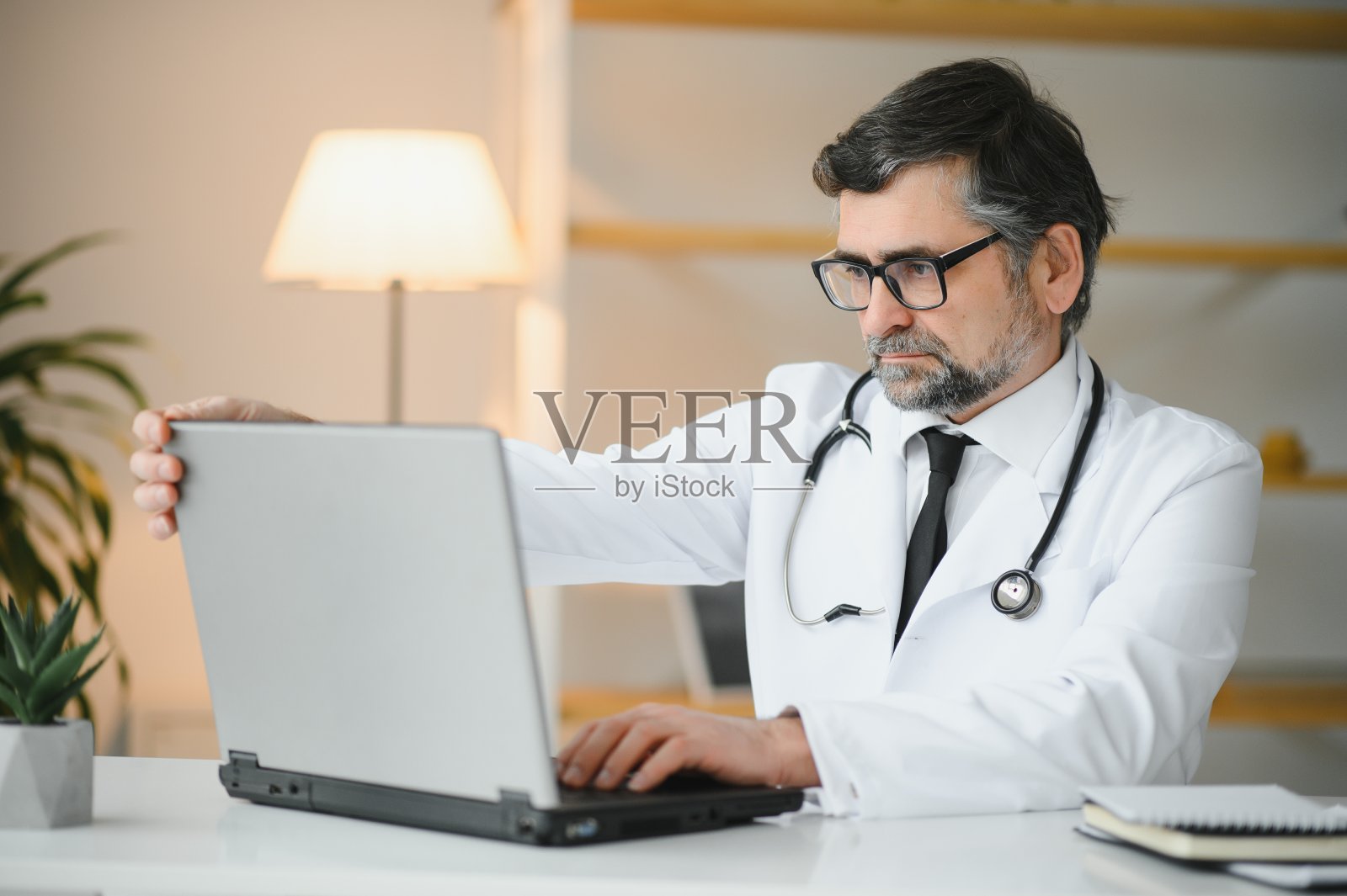 身穿白大褂的高级医生在工作场所的肖像。照片摄影图片