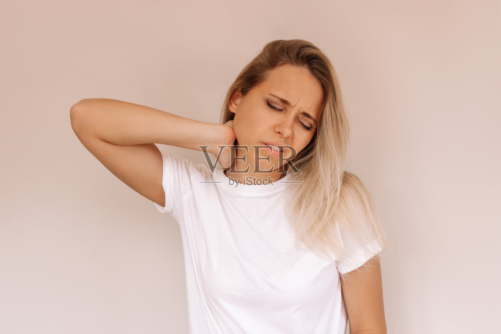 年轻有吸引力的白种人金发女人在一件白色t恤，脖子疼，抱着她的脖子照片摄影图片