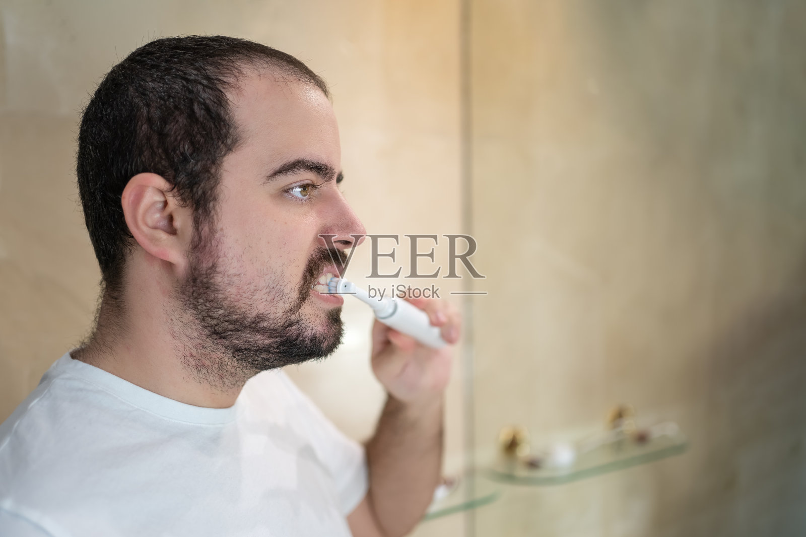 年轻的白人男子一边刷牙一边看着浴室的镜子，复印空间。照片摄影图片