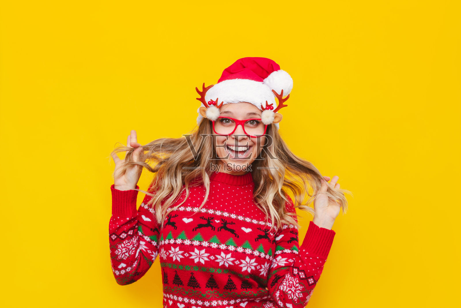 年轻快乐微笑的金发女人在圣诞红鹿毛衣和圣诞老人的帽子照片摄影图片