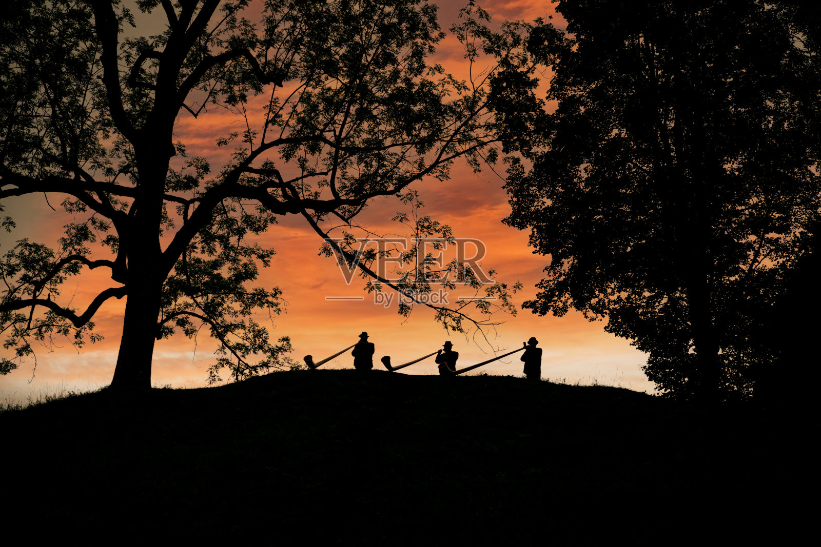 三个高地人在黄昏时弹奏trembitas。照片摄影图片
