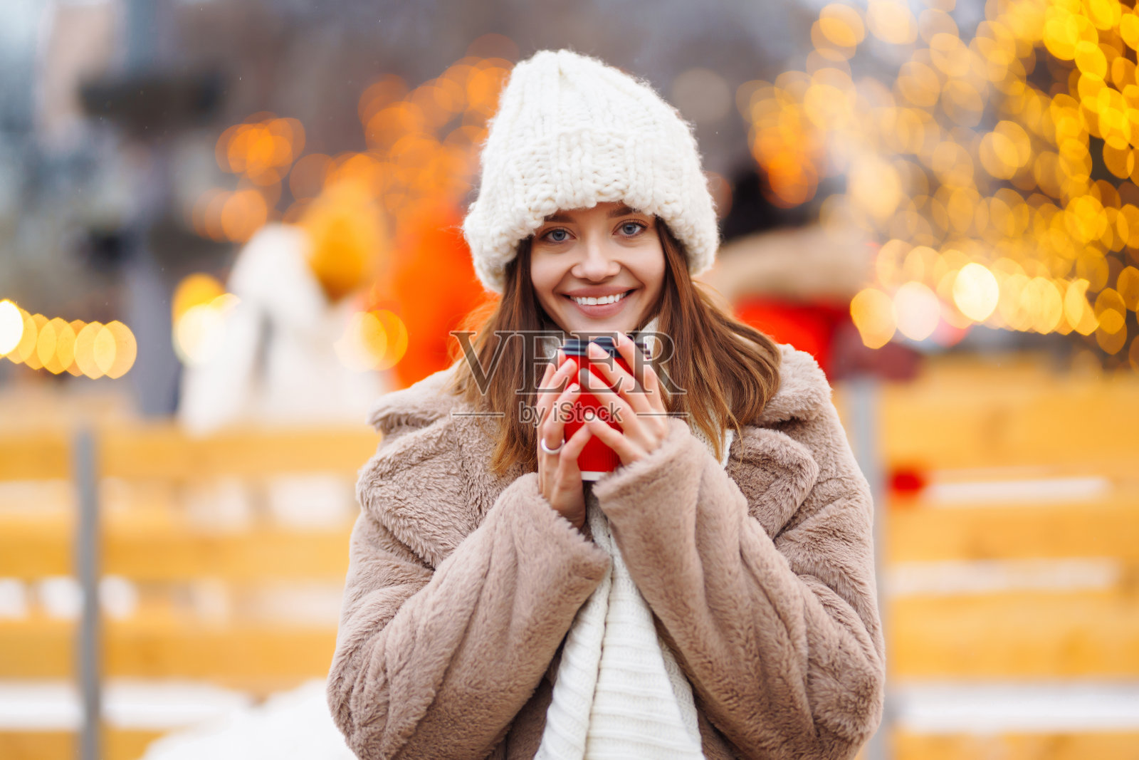 圣诞节，一个漂亮的女孩在集市上散步，喝着热饮照片摄影图片
