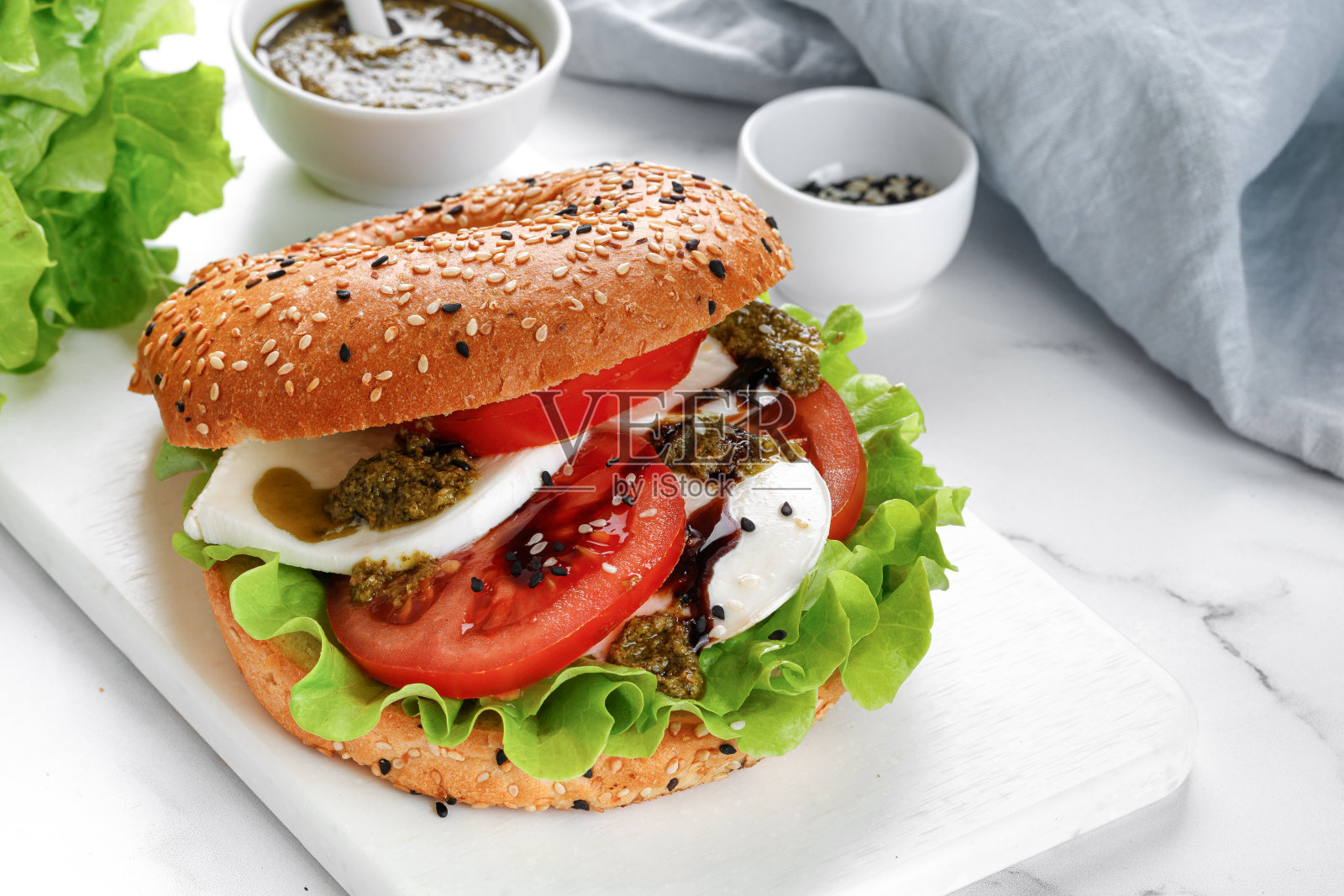 三明治，吐司，百吉饼加马苏里拉芝士，香蒜酱，西红柿。卡普里三明治放在白色砧板上。照片摄影图片