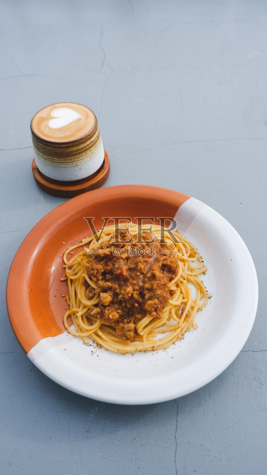 灰色的桌子上放着一盘健康的意大利面条，上面撒着美味的番茄和牛肉肉酱，还有新鲜的罗勒。配卡布奇诺照片摄影图片