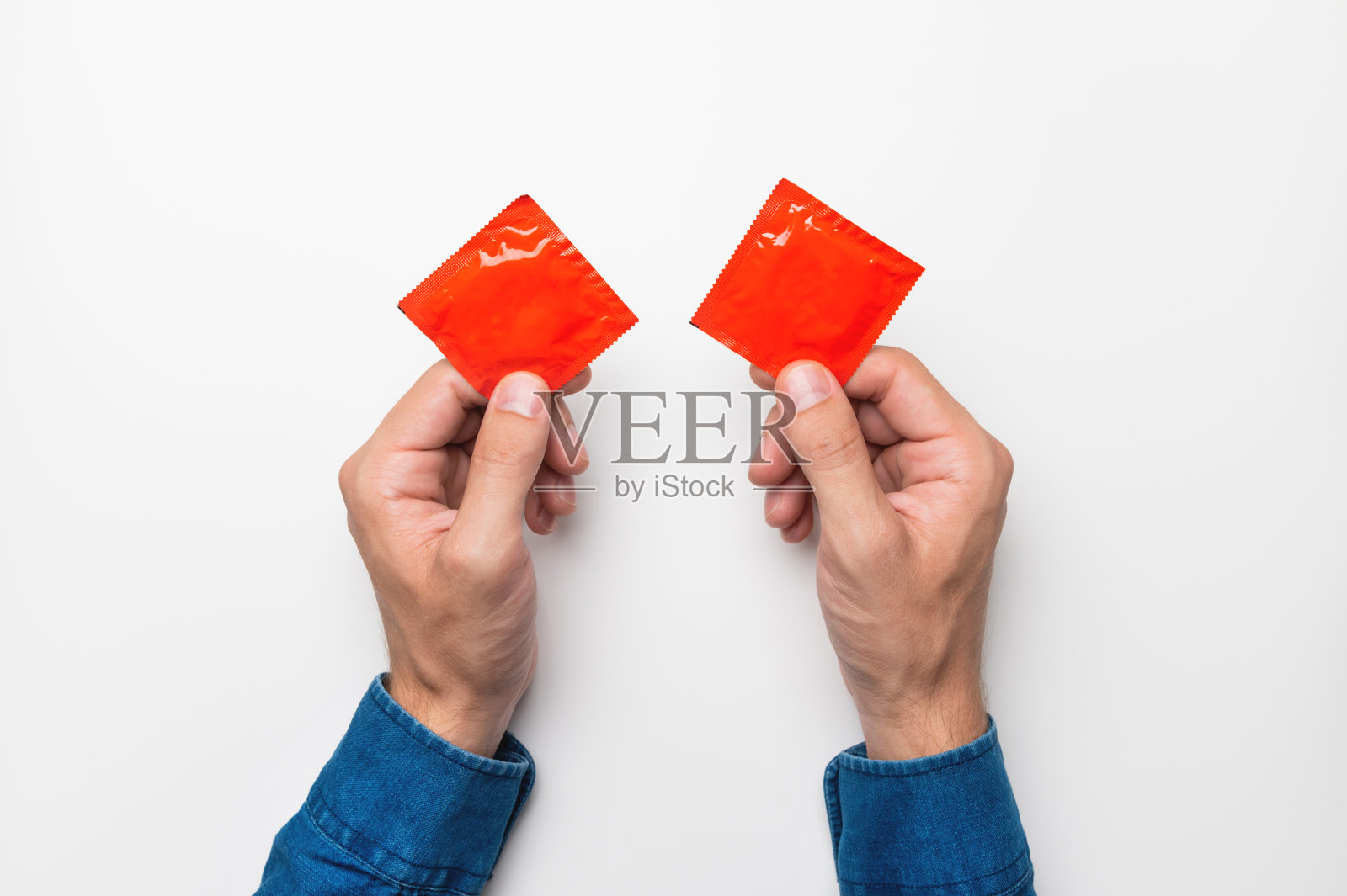 两个男性的手拿着带有避孕套的红色包裹，俯视图在白色背景上。性商店横幅的模型照片摄影图片