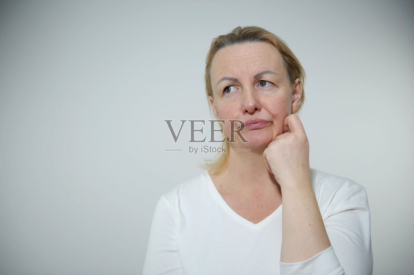 成年女子心烦意乱，不满意，她看向别处，把手放在脸颊上，撅起嘴唇，悲伤的眼睛低了下来，现在她会哭，她没有发型，没有化妆，大量的家庭作业，真正的普通女人照片摄影图片