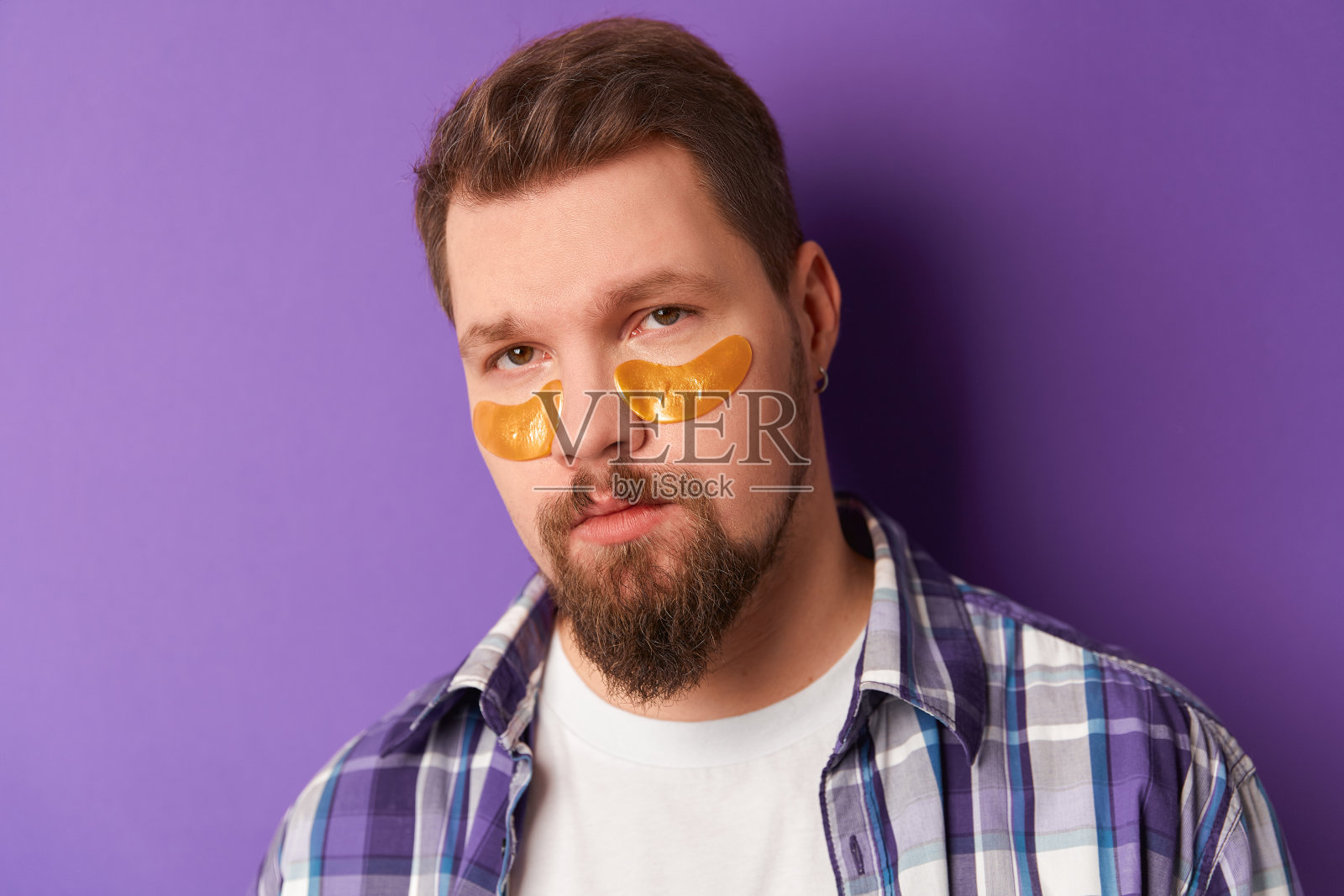 一个穿着白色t恤，戴着眼罩的男人站在紫罗兰色的背景下。美容水疗健康理念照片摄影图片