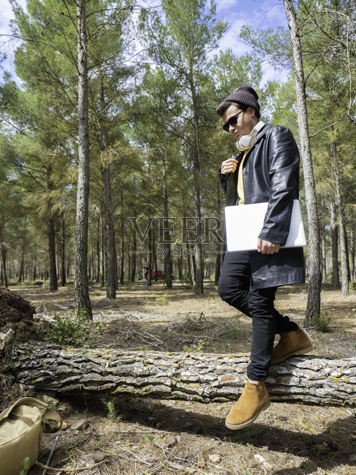 一个戴着帽子和墨镜的少年，拿着笔记本电脑站在公园里照片摄影图片