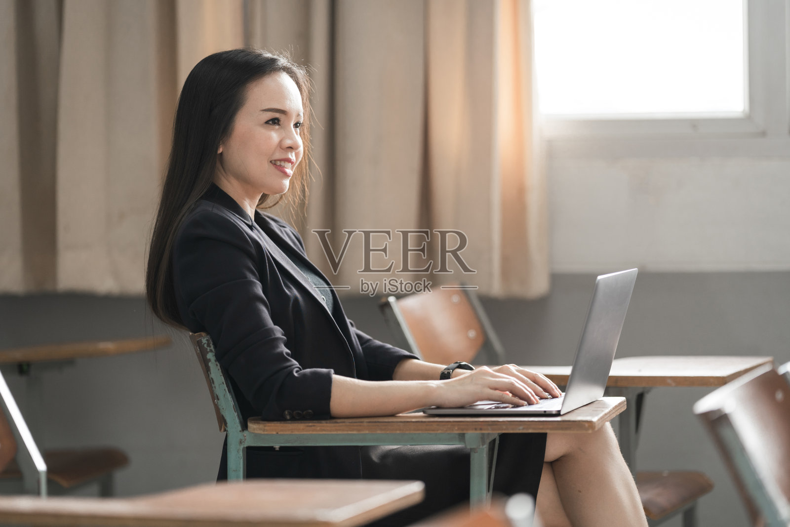女老师穿着黑色西装，在教室里拿着一台笔记本电脑照片摄影图片