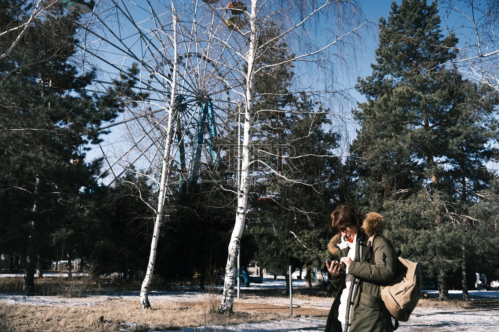 开朗成熟的女子在阳光明媚的冬日公园里使用手机照片摄影图片