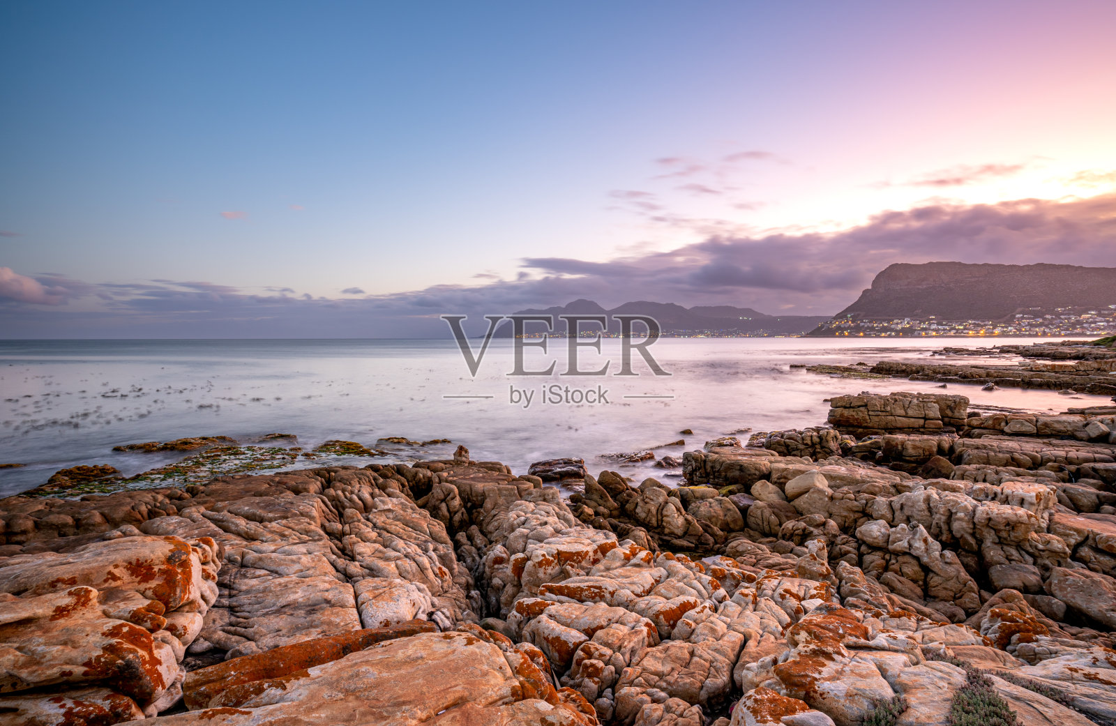 在南非开普敦外的开普半岛的福斯湾，鱼虎克的岩石海岸线上的海浪与充满活力的日落照片摄影图片